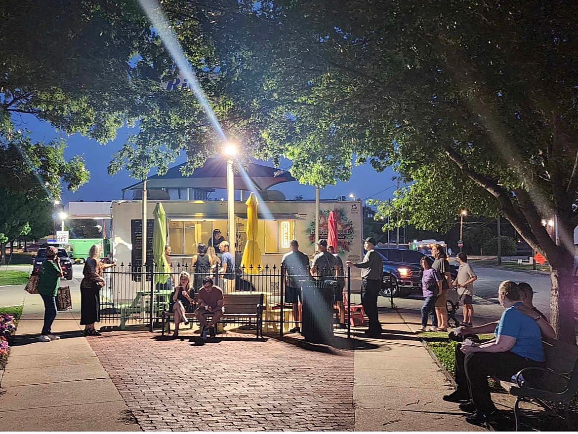 People gathered around Pop-Pop Feducchi’s lit trailer patio beneath large trees at night
